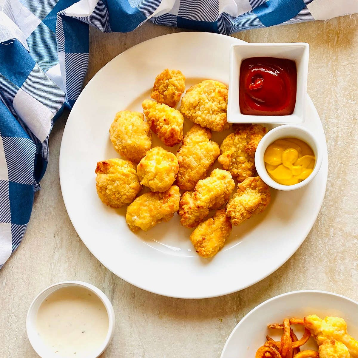 frozen chicken nuggets cooked in air fryer on a plate with ketchup and mustard for dipping