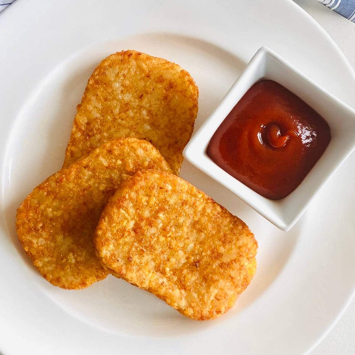 air fryer hash brown patties on a plate with ketchup
