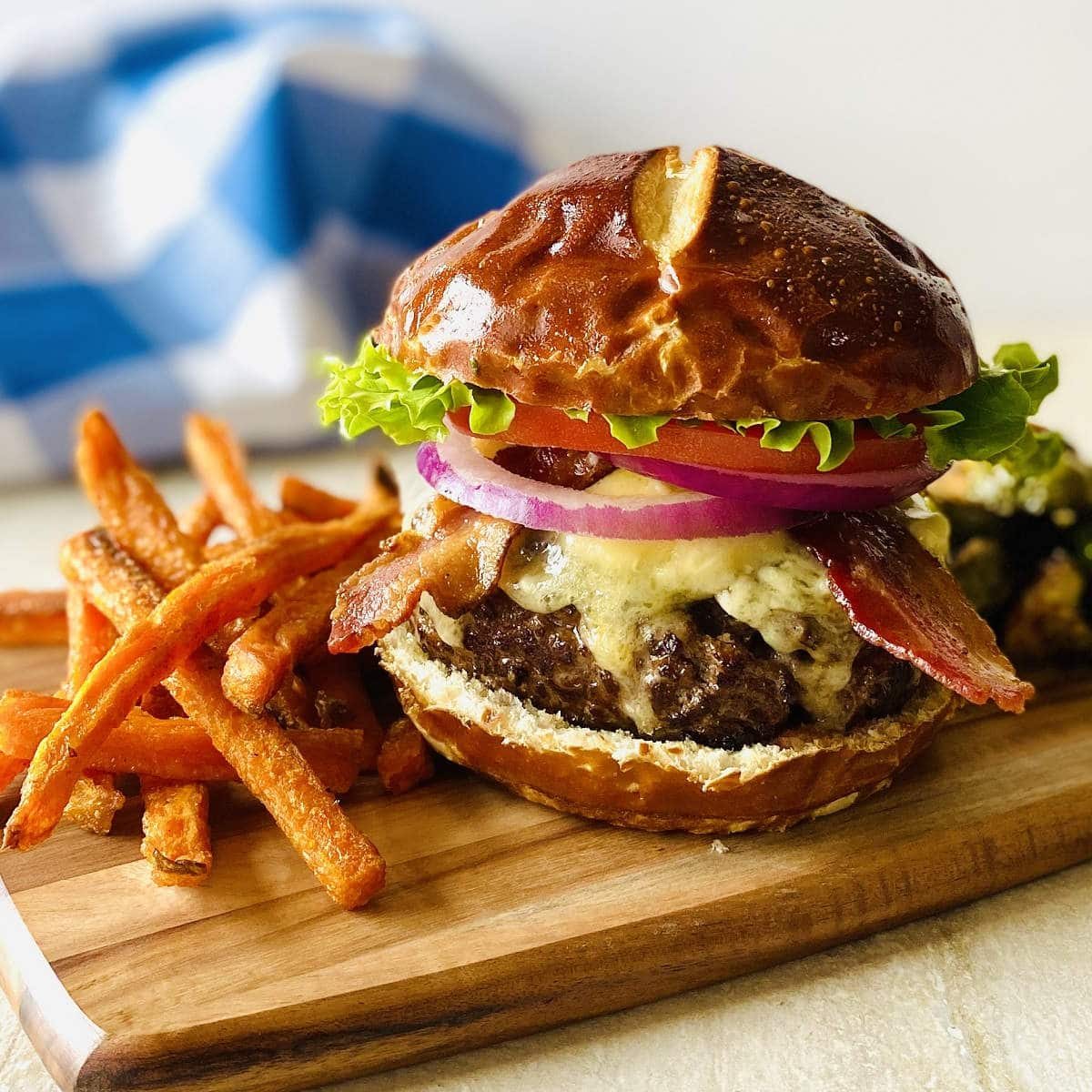 american wagyu burger on cutting board next to sweet potato fries