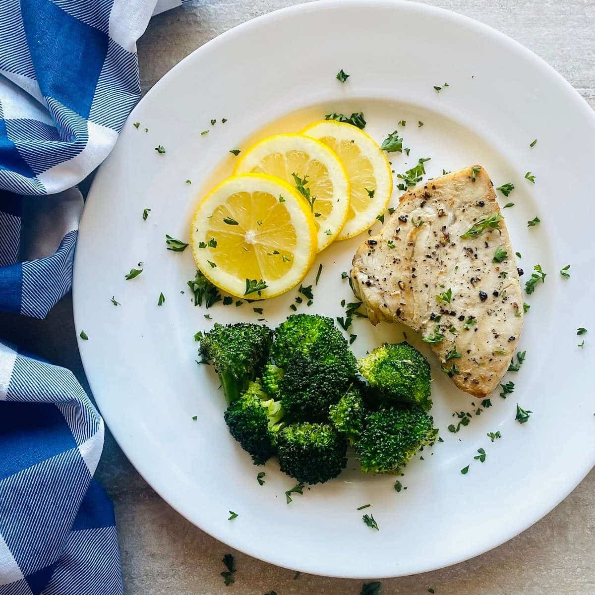 best air fryer swordfish recipe on a plate with lemon slices, and broccoli