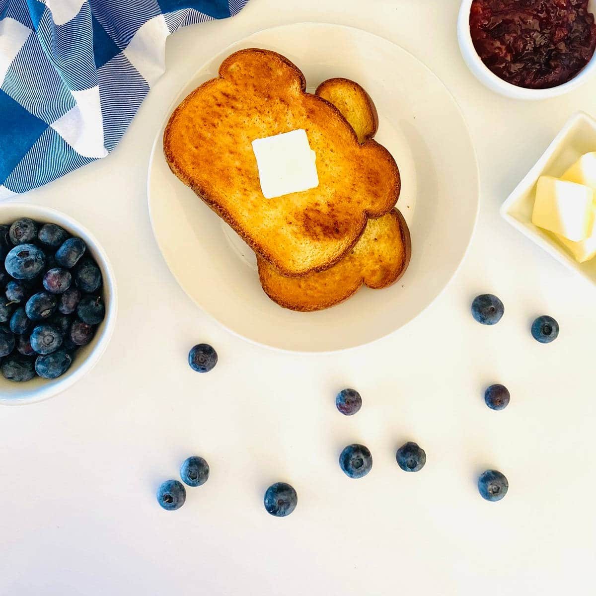 ninja air fryer toast on plate topped with butter and sitting next to a dish of jam and butter