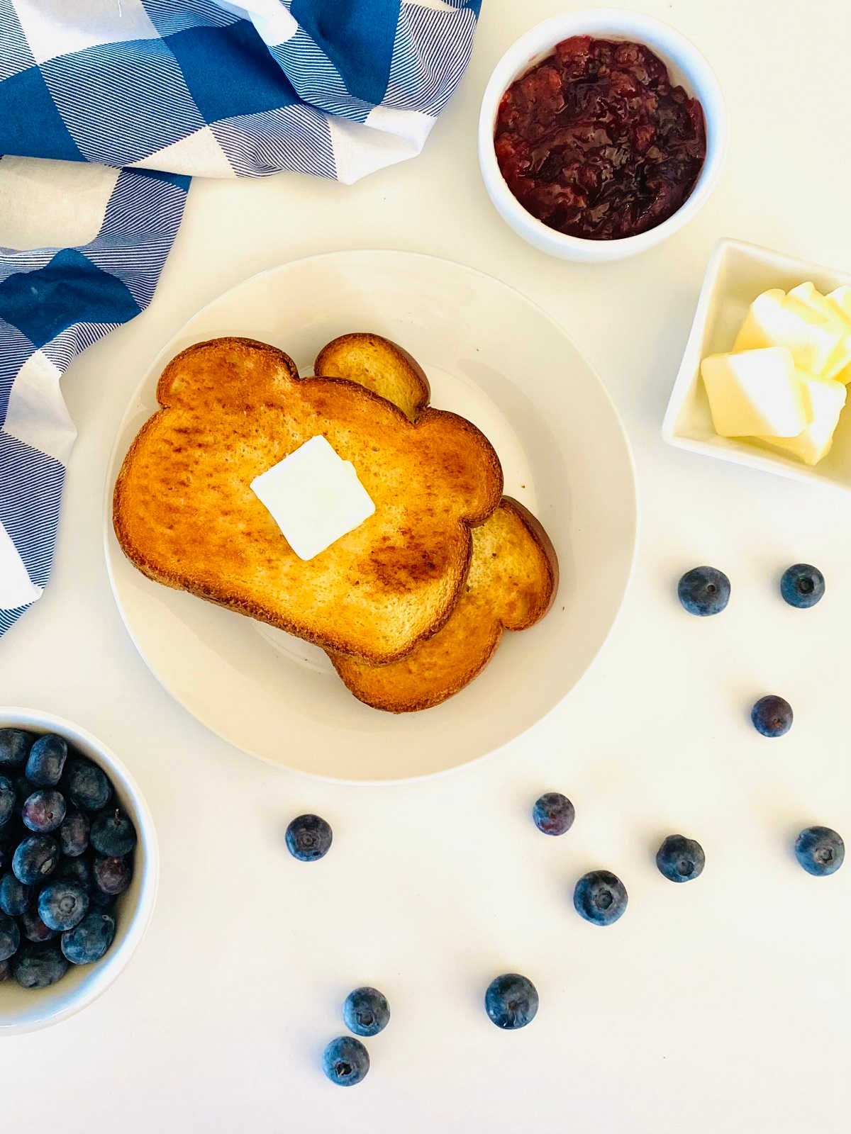 toast cooked in air fryer oven on plate topped with butter and sitting next to a dish of jam and butter