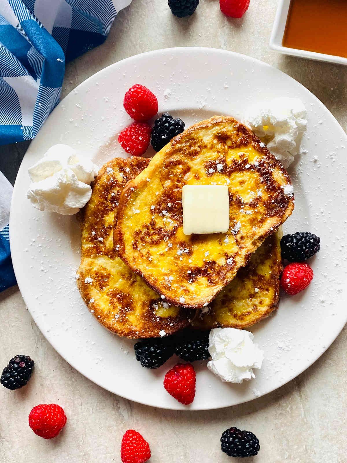 protein french toast on a plate with berries, powdered sugar, butter, whipped cream and sugar free syrup