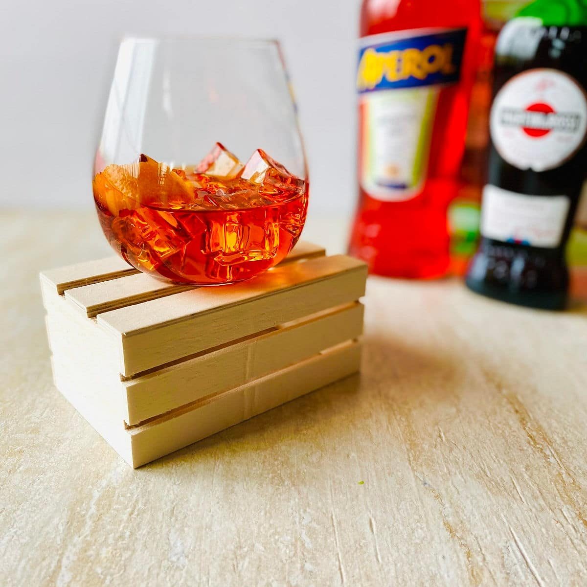 aperol negroni cocktail in a glass with ice, an orange peel and aperol, vermouth and gin in the background