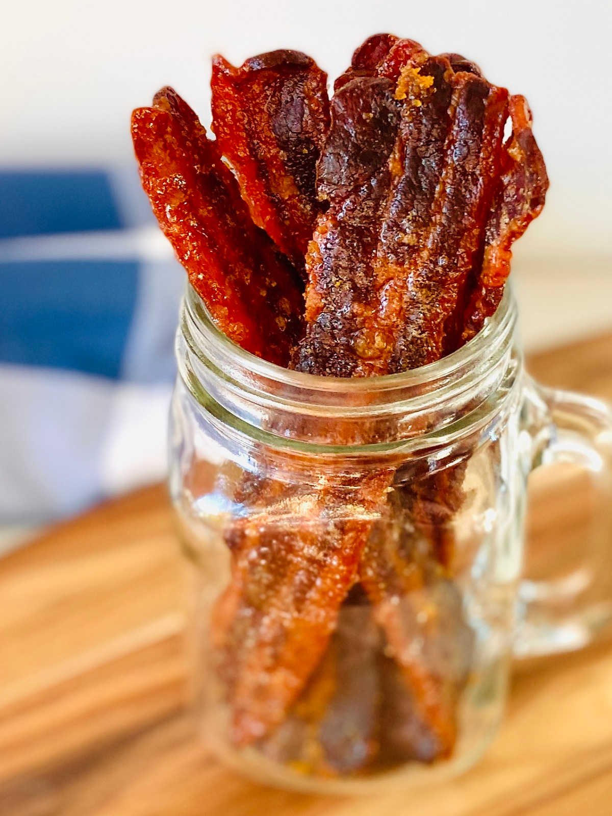maple bacon jerky sitting upright in glass jar with blue napkin in background
