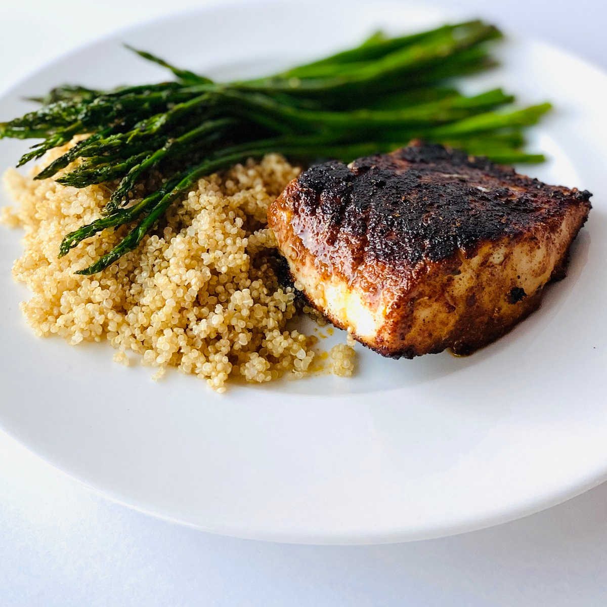 blackened cod on a plate next to quinoa and roasted asparagus