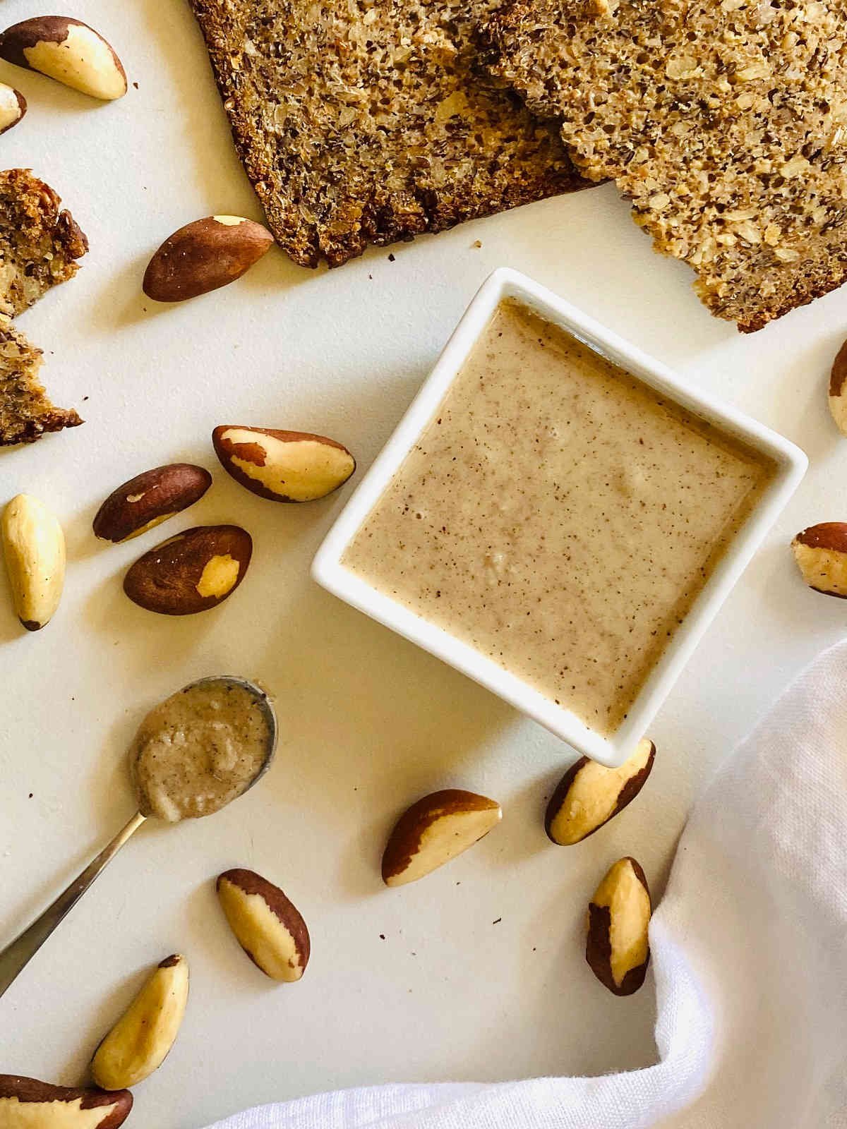 brazil nut butter in white dish next to bread, spoon and napkin