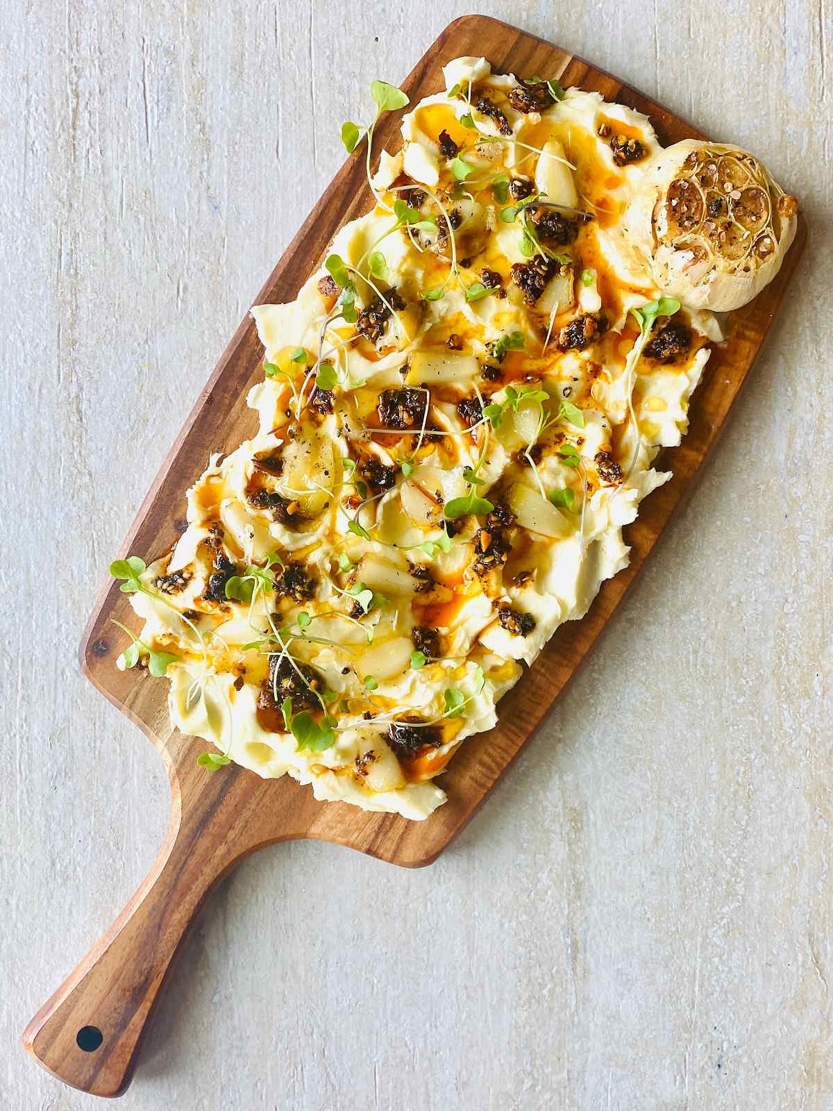viral tik tok butter board with butter, garlic, salt, chili crisp oil, honey and microgreens with a whole roasted garlic in the corner.