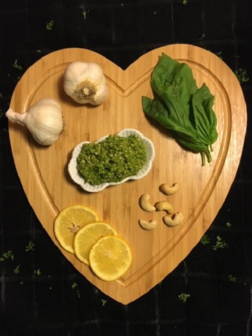 cashew basil pesto on cutting board surrounded by garlic lemon cashews and basil