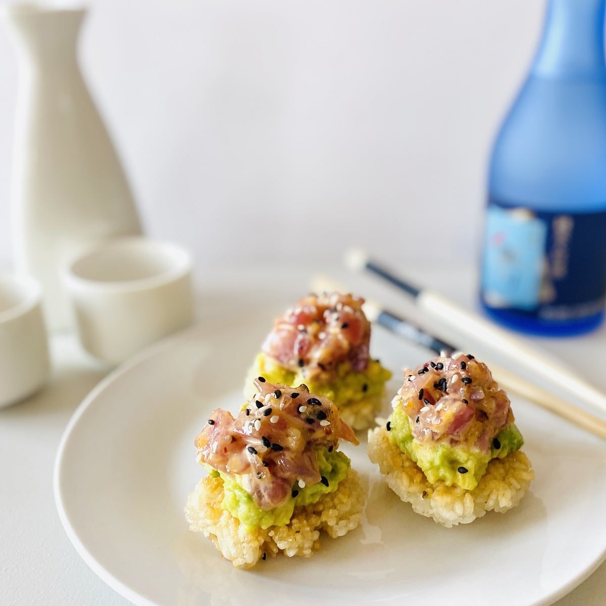 spicy tuna crispy rice on plate next to chopsticks, sake and sake carafe and glasses