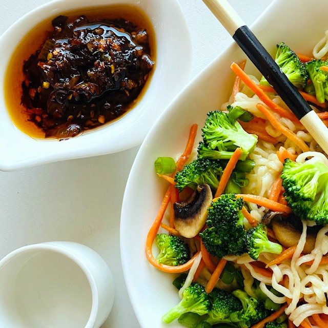 chili-crisp-in-dish-and-bowl-of-noodles-vegetables-and-chopsticks