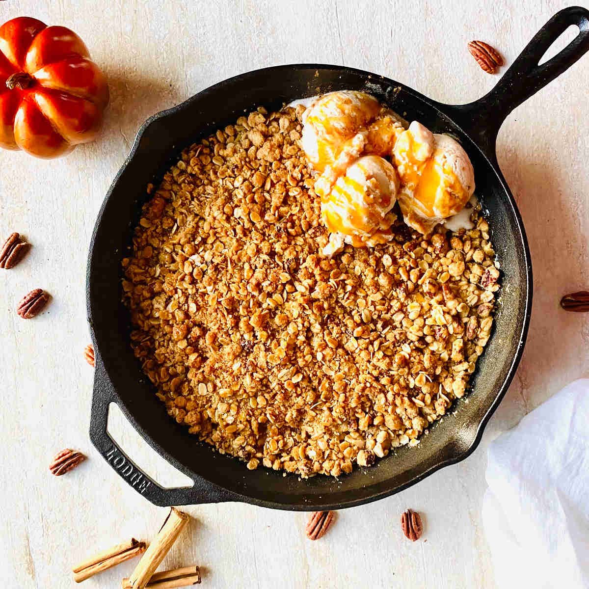 cast iron skillet apple crisp with ice cream next to pecans and a pumpkin