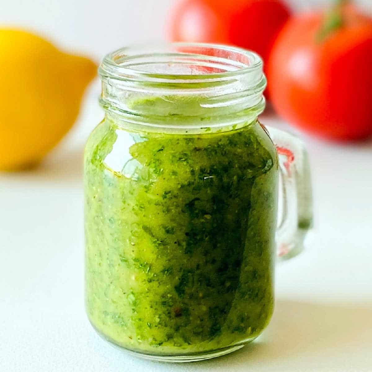 cilantro dressing in cup with tomato and lemon in background