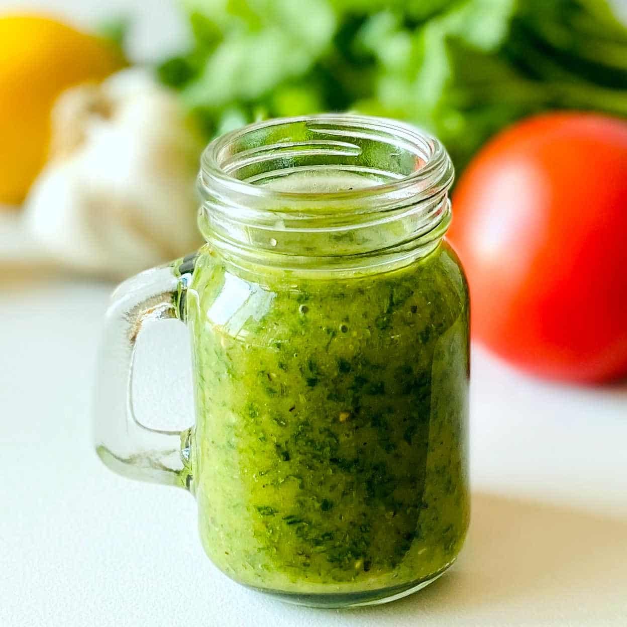 cilantro dressing in cup with tomato cilantro garlic and lemon in background