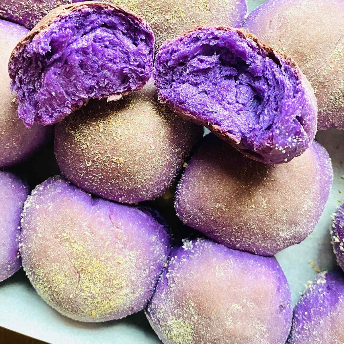 ube pandesal roll torn in half sitting on tray of freshly baked ube pandesal