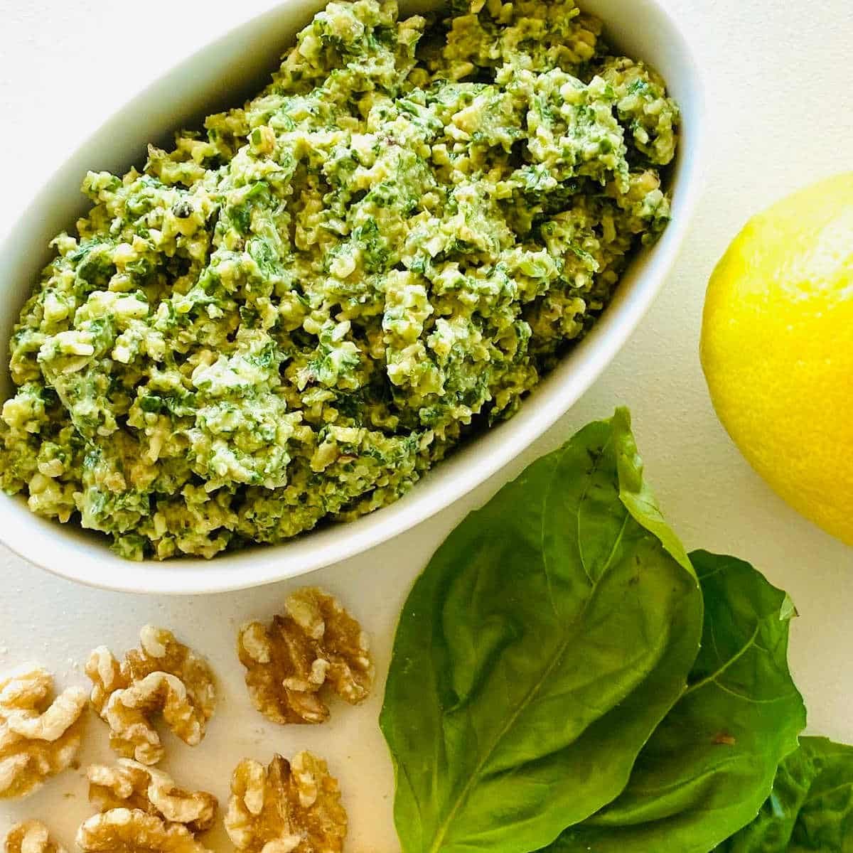 pesto recipe without pine nuts next to walnuts, basil and fresh lemon.
