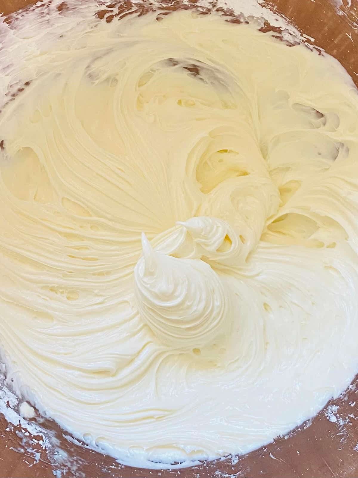 process shot for how to make cream cheese frosting for cinnamon rolls.