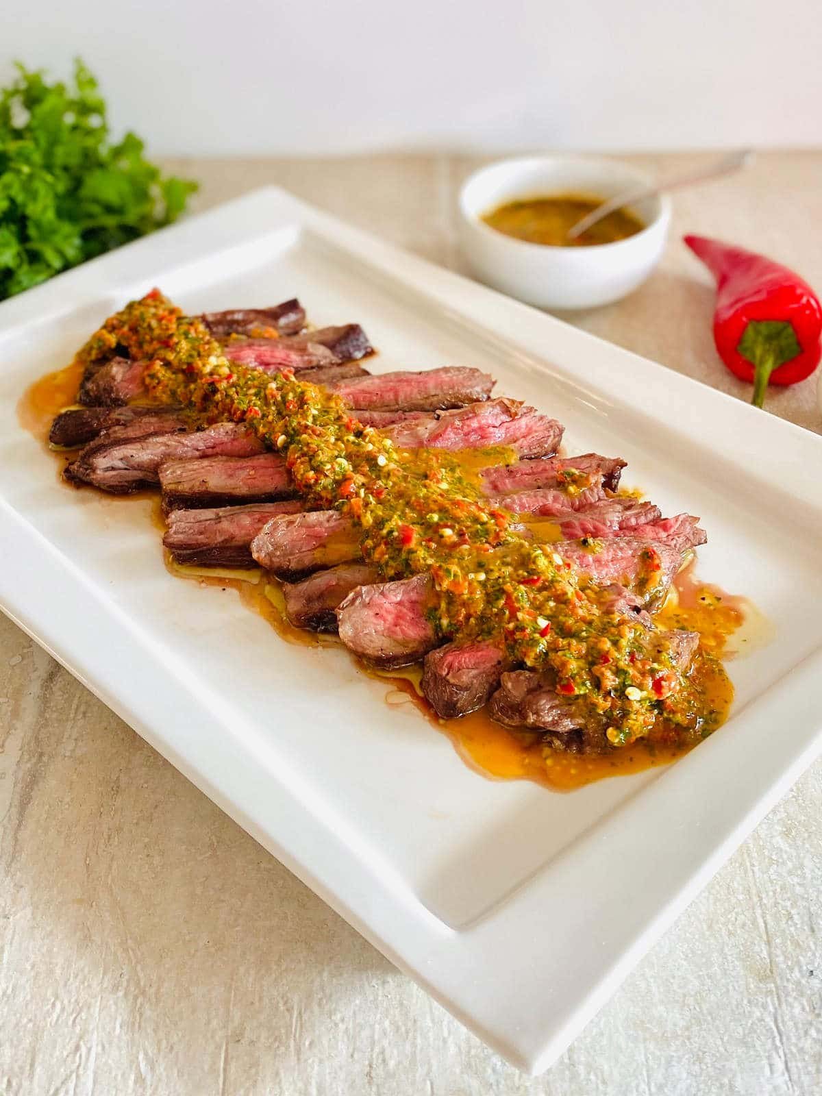 wagyu denver steak sliced on a plate with red pepper and chimichurri in the background