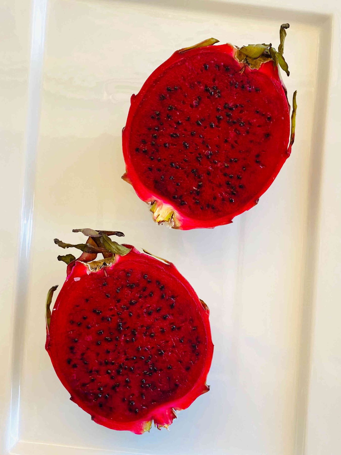 red dragon fruit sliced in half on a white rectangular plate