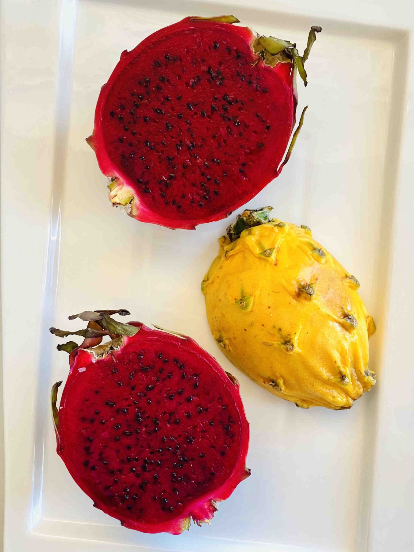 red dragon fruit and yellow dragon fruit sliced in half on a white rectangular plate
