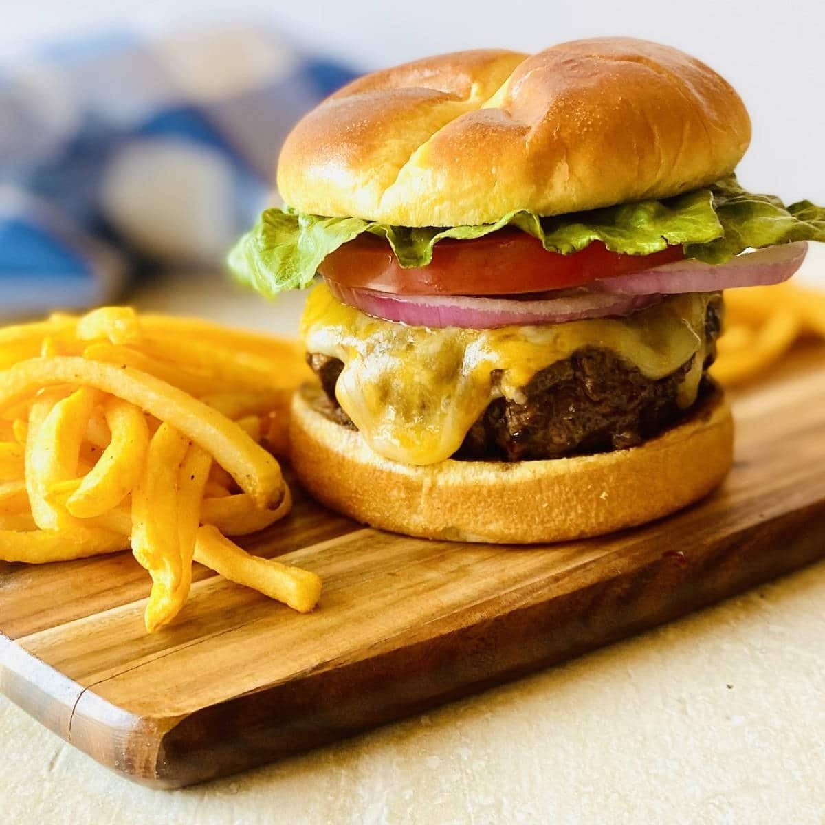 elk burger on a wooden platter next to french fries