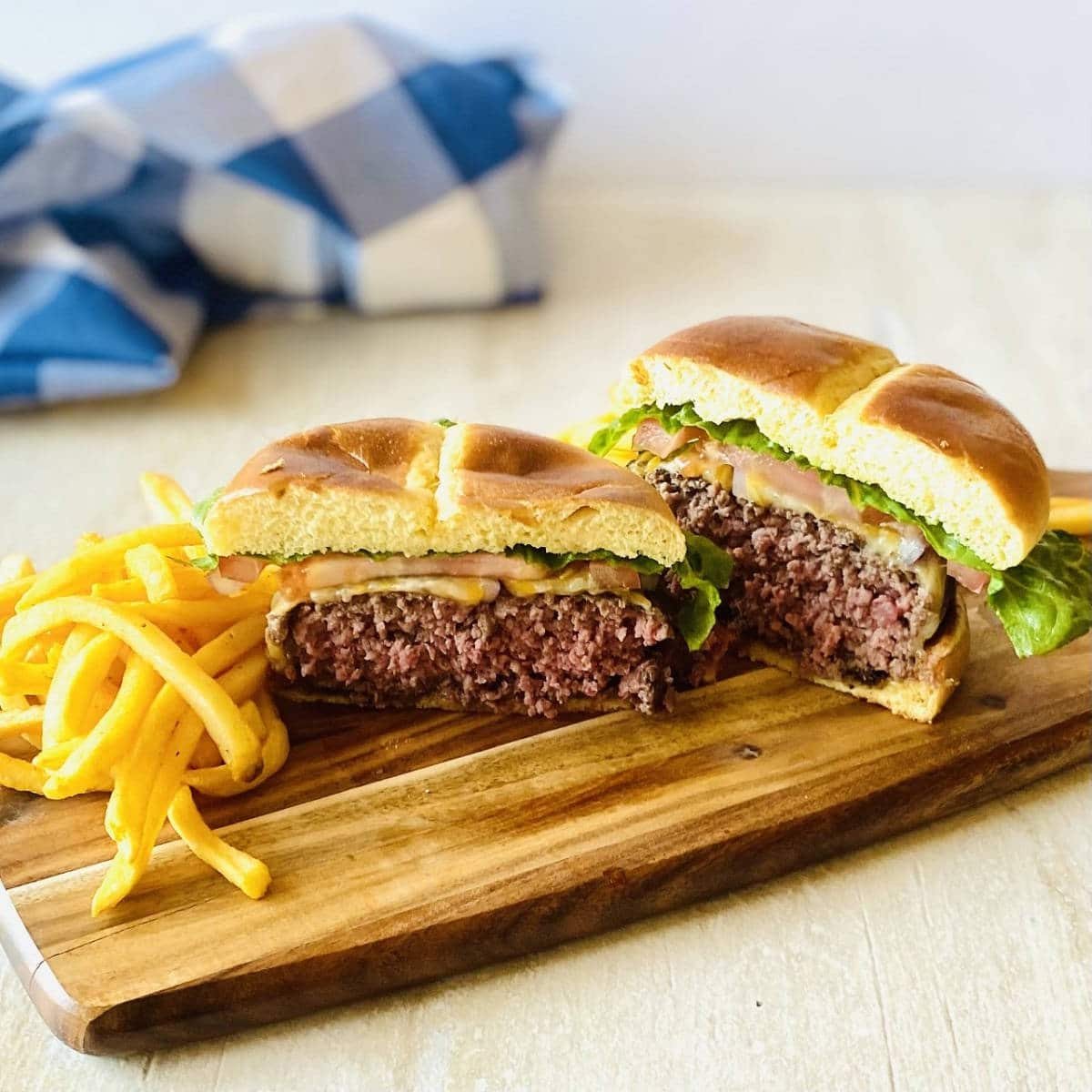elk burgers cut in half on a wooden platter next to french fries
