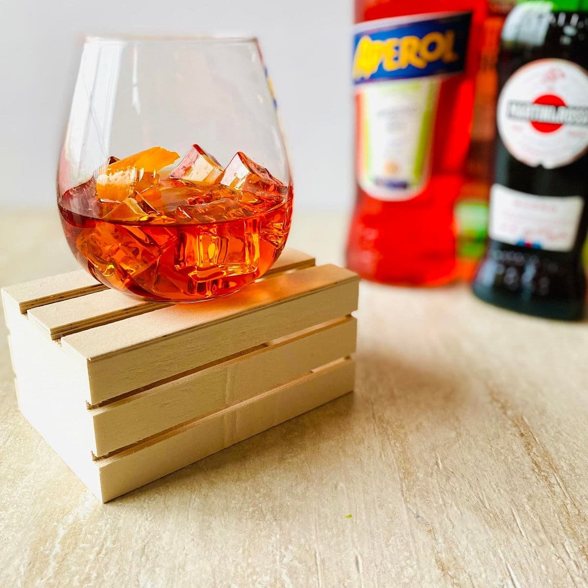 Aperol Negroni cocktail in a glass with ice, an orange peel and aperol, vermouth and gin in the background