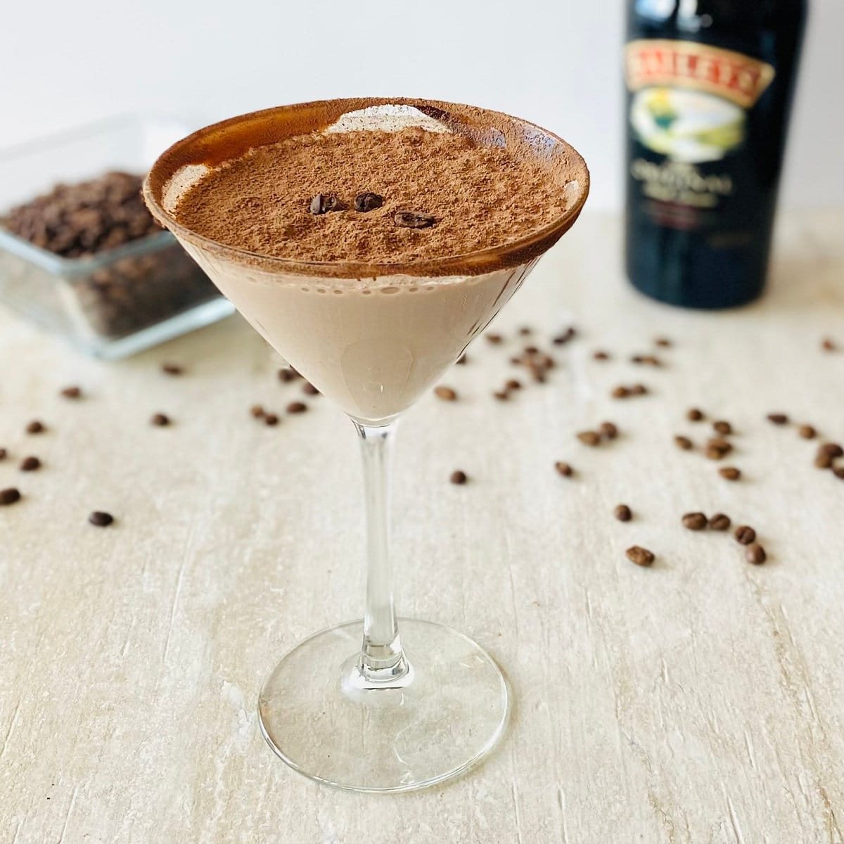 kahlua espresso martini in martini glass with baileys and espresso beans in the background