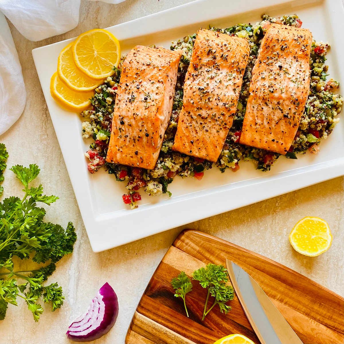 three cooked pieces of Faroe Island salmon filets on a bed of greens next to a cutting board
