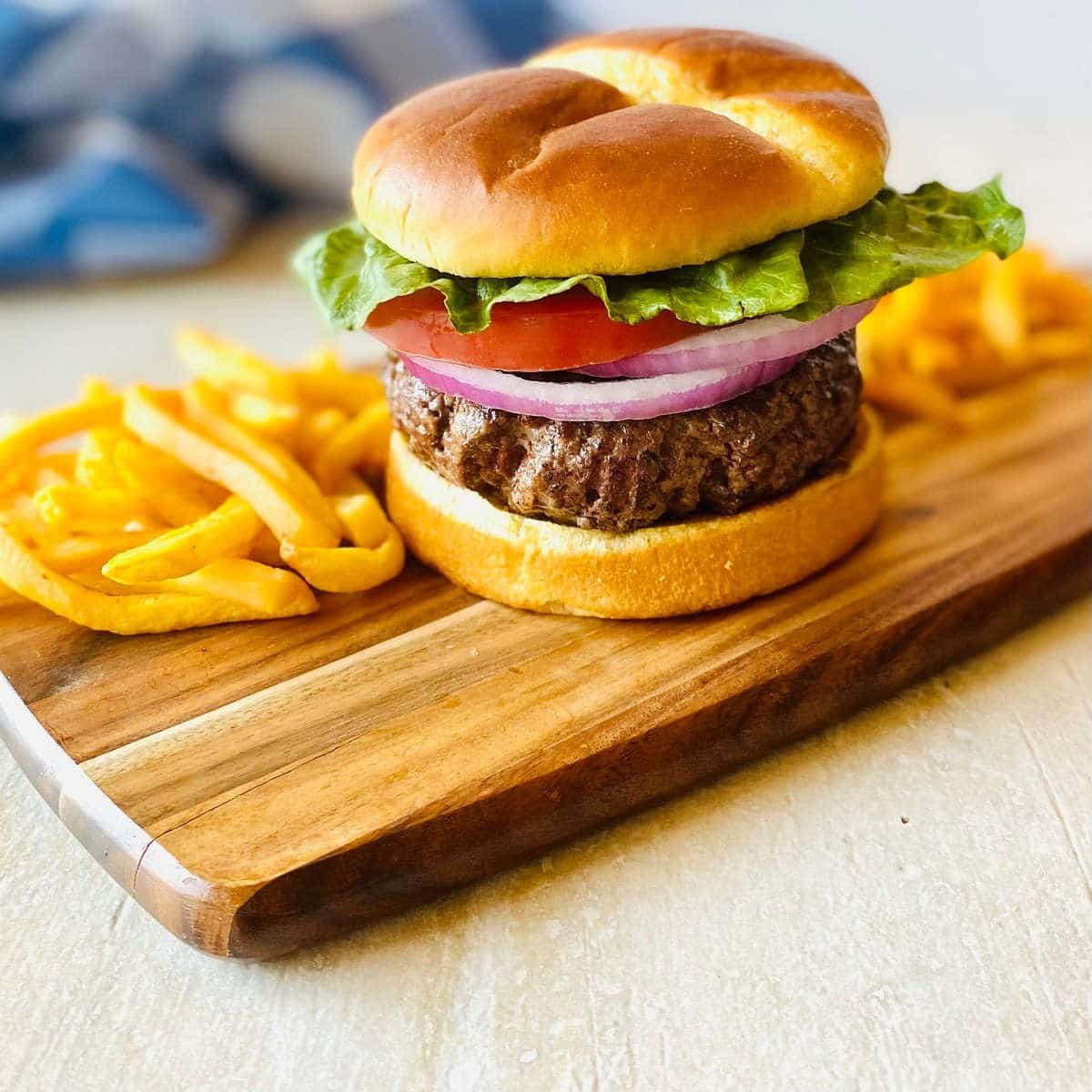 hamburger cooked frozen in air fryer on a cutting board with french fries