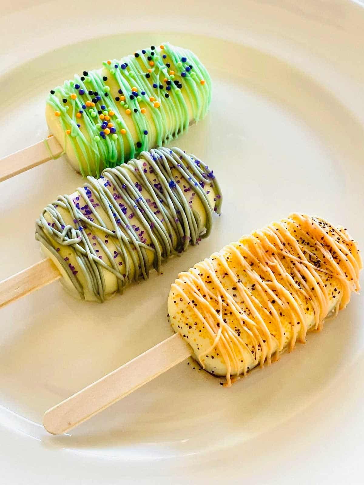 three halloween cake popsicles on a plate decorated with sprinkles