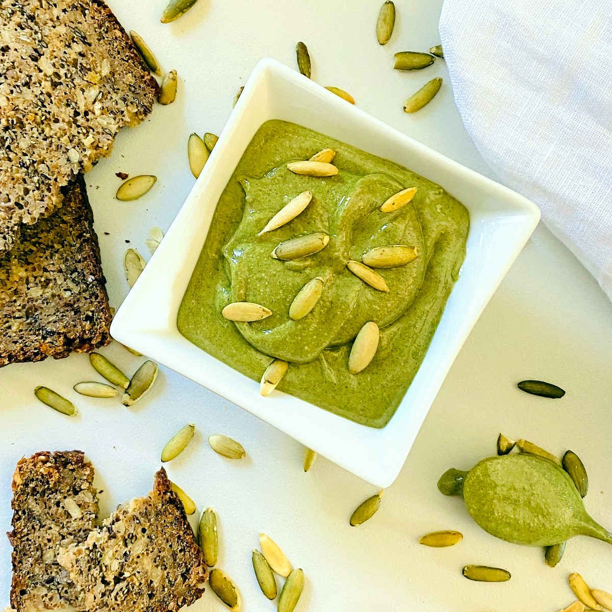pumpkin seed butter in white dish next to spoon, bread and napkin