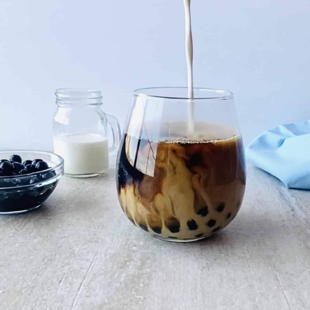 hokkaido milk being poured into hokkaido milk tea with boba in the background