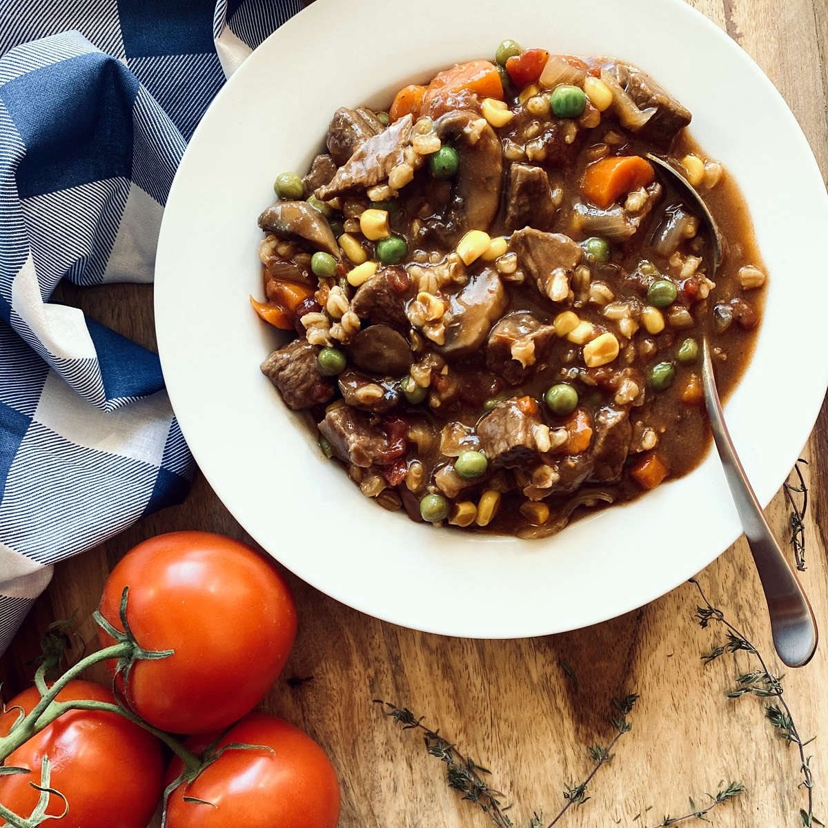 instant pot vegetable beef soup in white bowl with spoon next to napkin, tomatoes and herbs