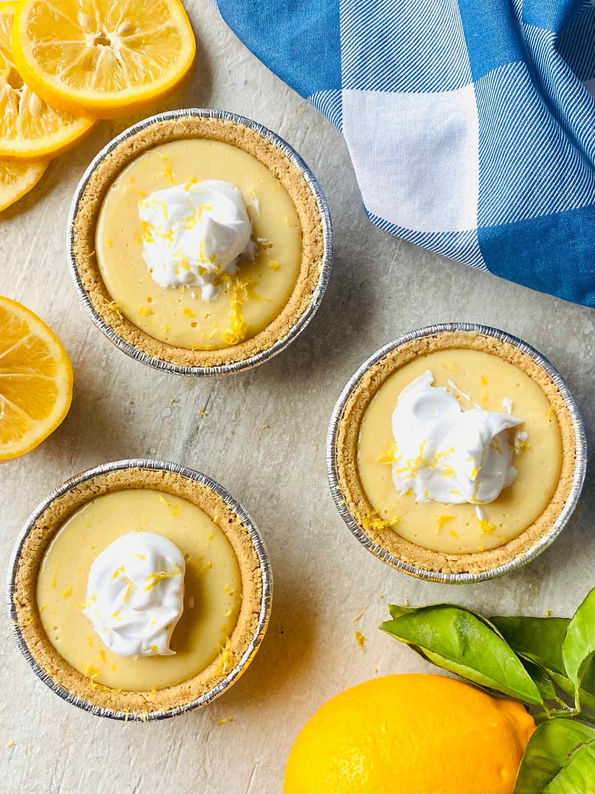 mini lemon pie with graham cracker crust garnished with whipped cream next to a fresh lemon.
