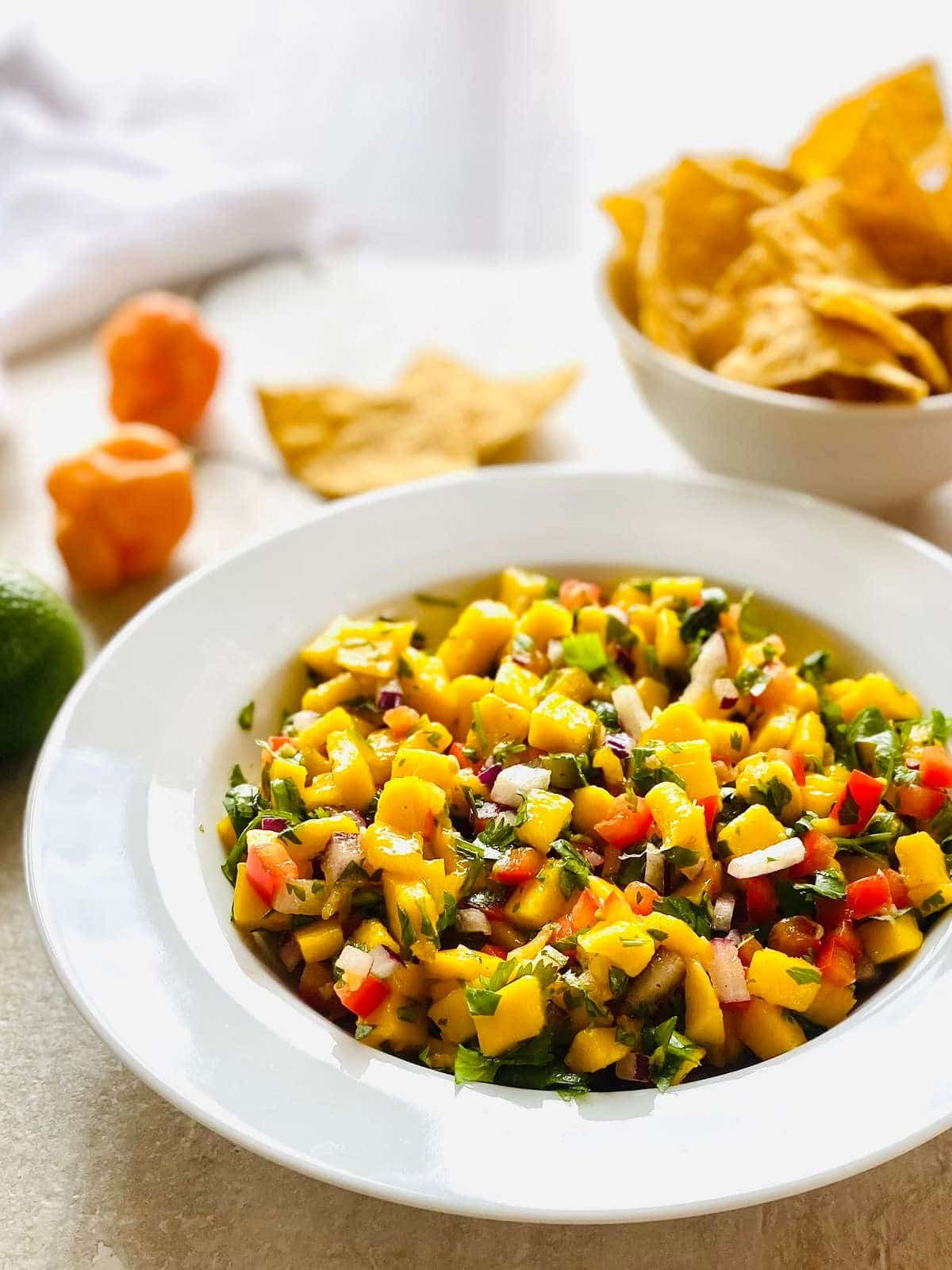 habanero mango salsa in a bowl and a bowl of tortilla chips and habanero peppers in the background