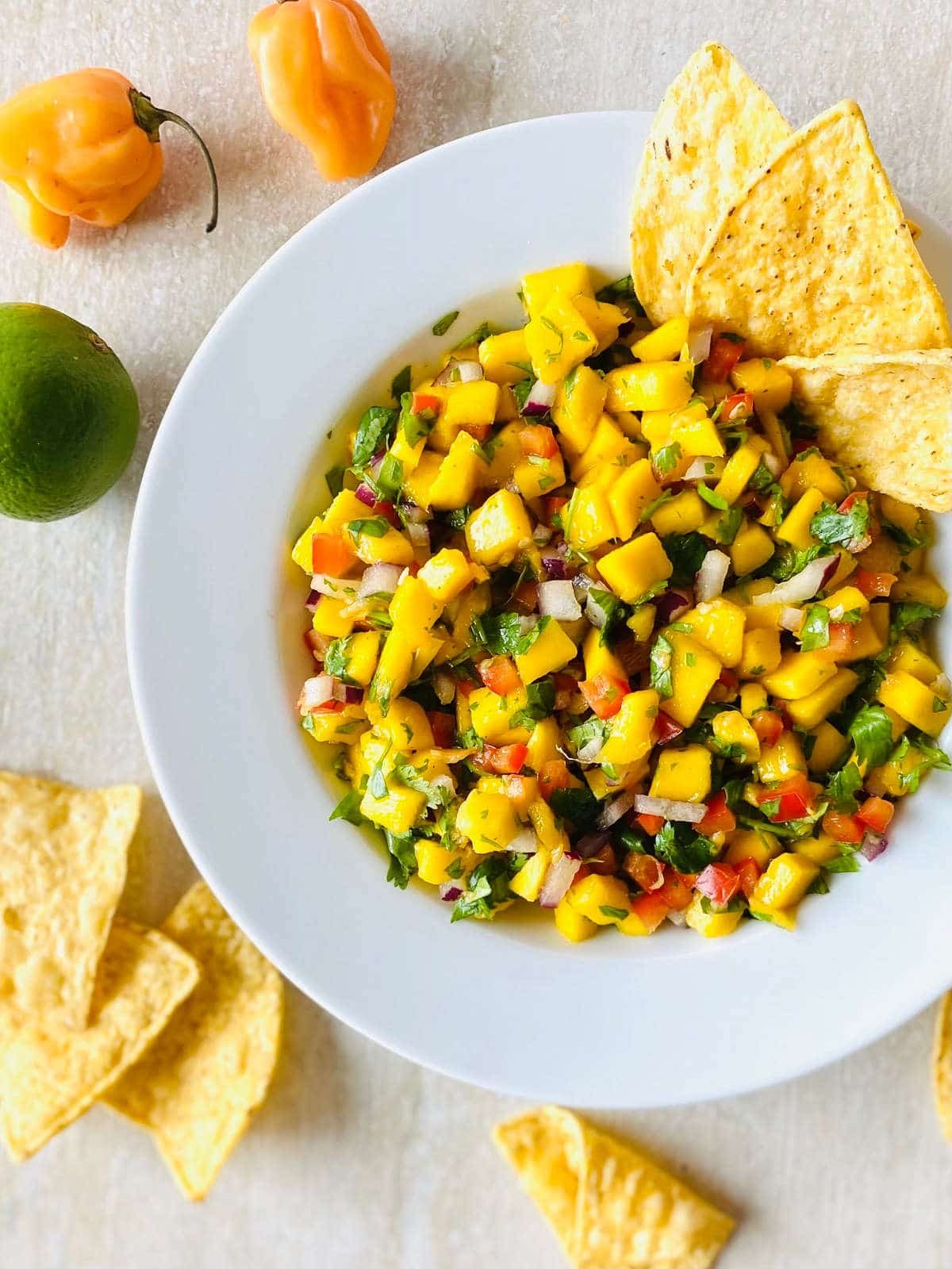mango habanero salsa in a bowl with chips in the salsa next to habanero peppers