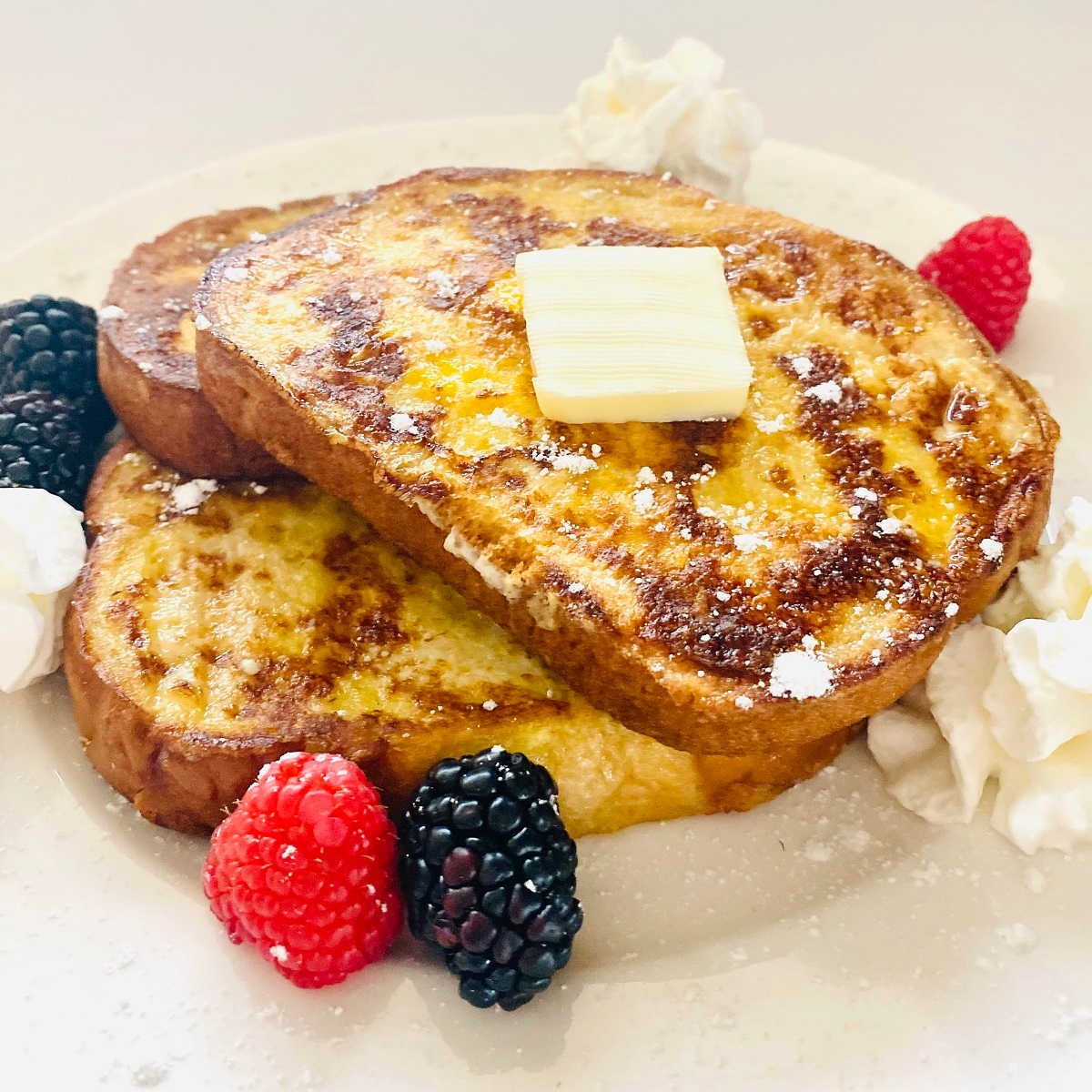 protein french toast with slice of butter, raspberries, blackberries and whipped cream