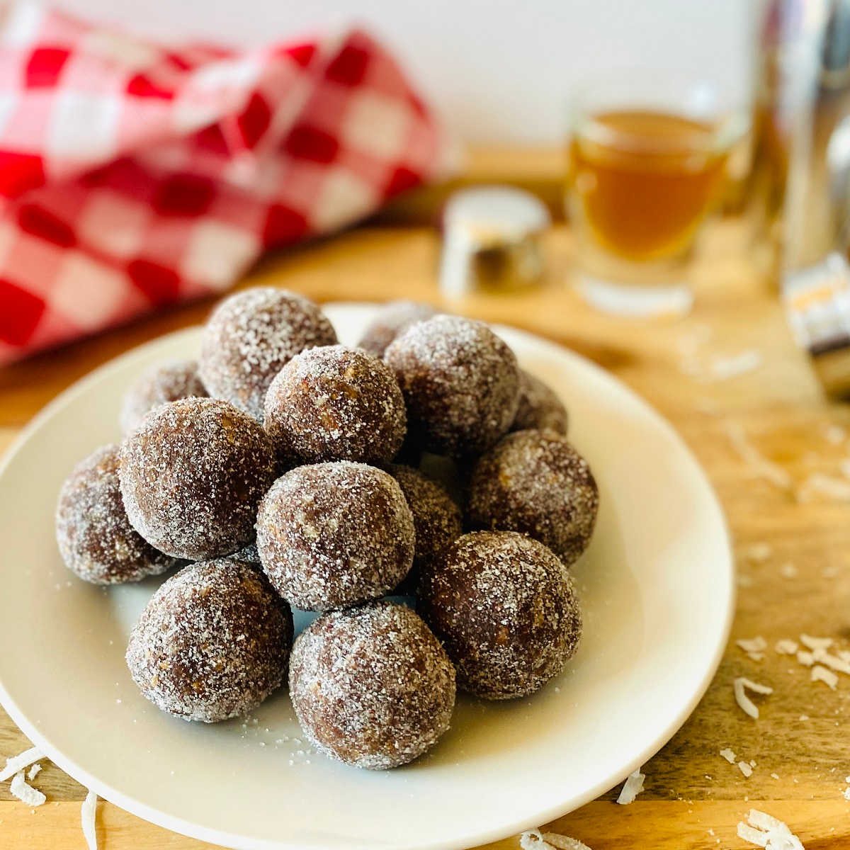 coconut rum balls on a plate next with red linen and shot of rum in the background