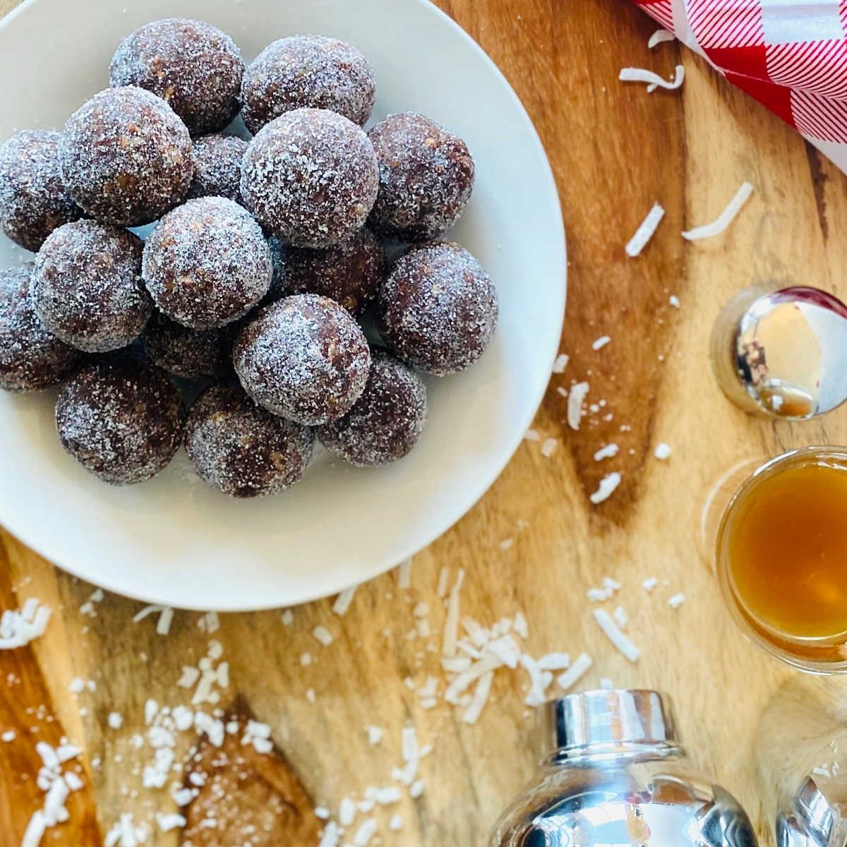 coconut rum balls on a plate next to rum shot, martini shaker and red linen