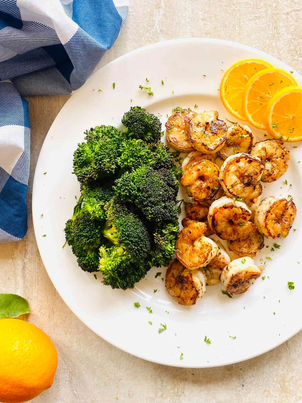 pan seared citrus shrimp on a plate with broccoli and lemon.