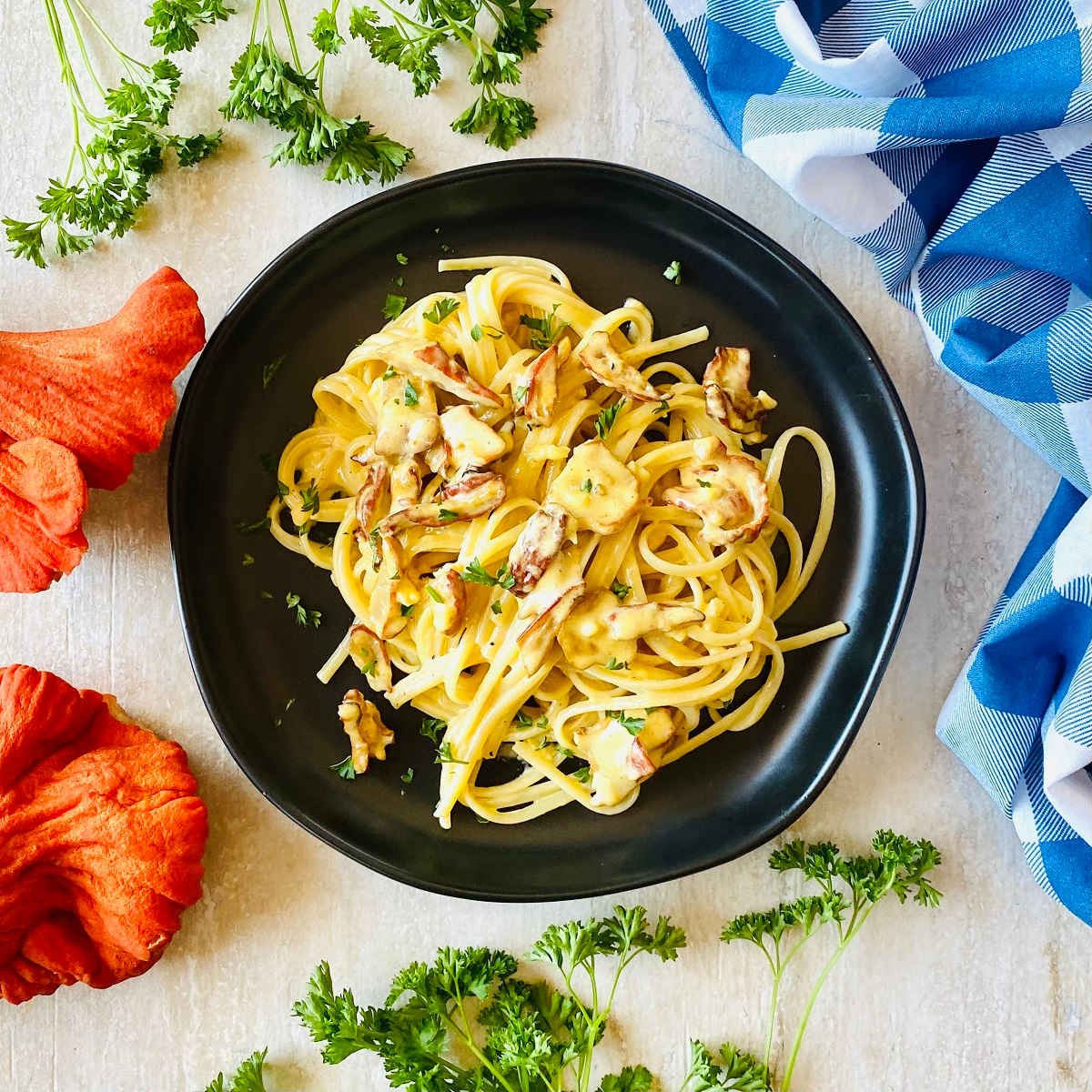 lobster mushroom recipe on a black plate next to fresh lobster mushrooms, parsley and a blue napkin