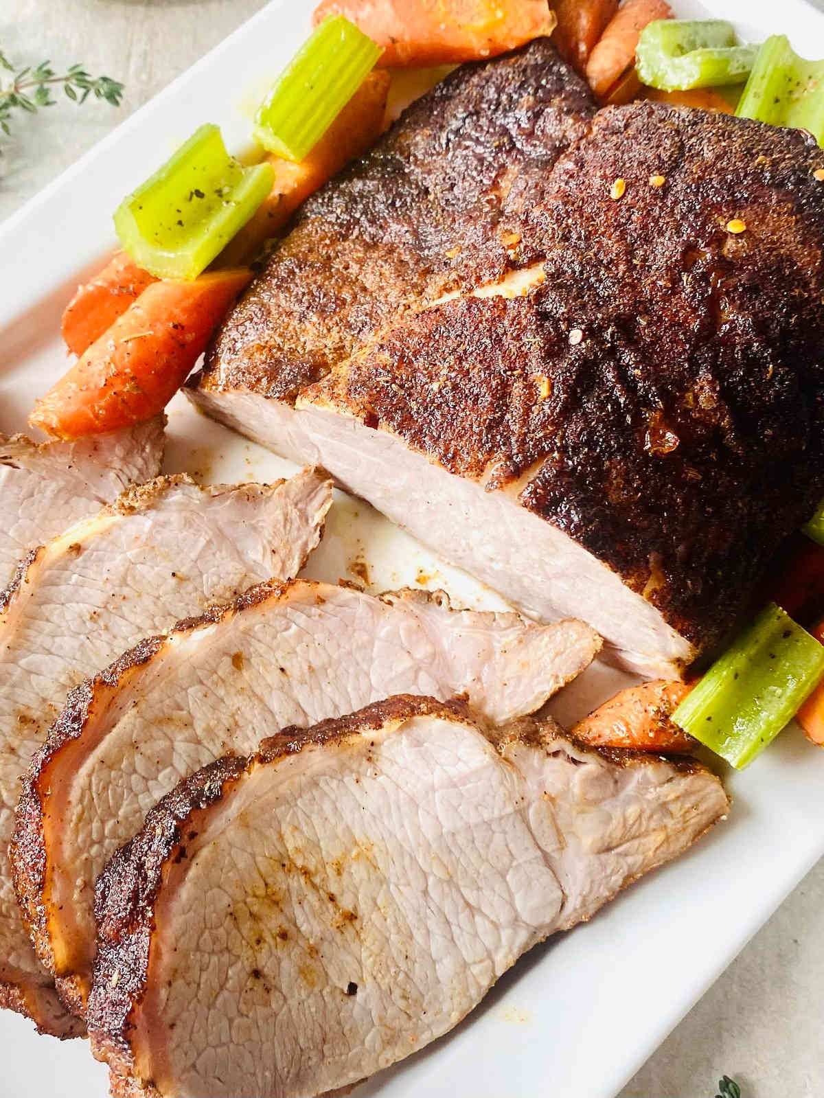 traeger smoked pork loin on plate surrounded by roasted vegetables.