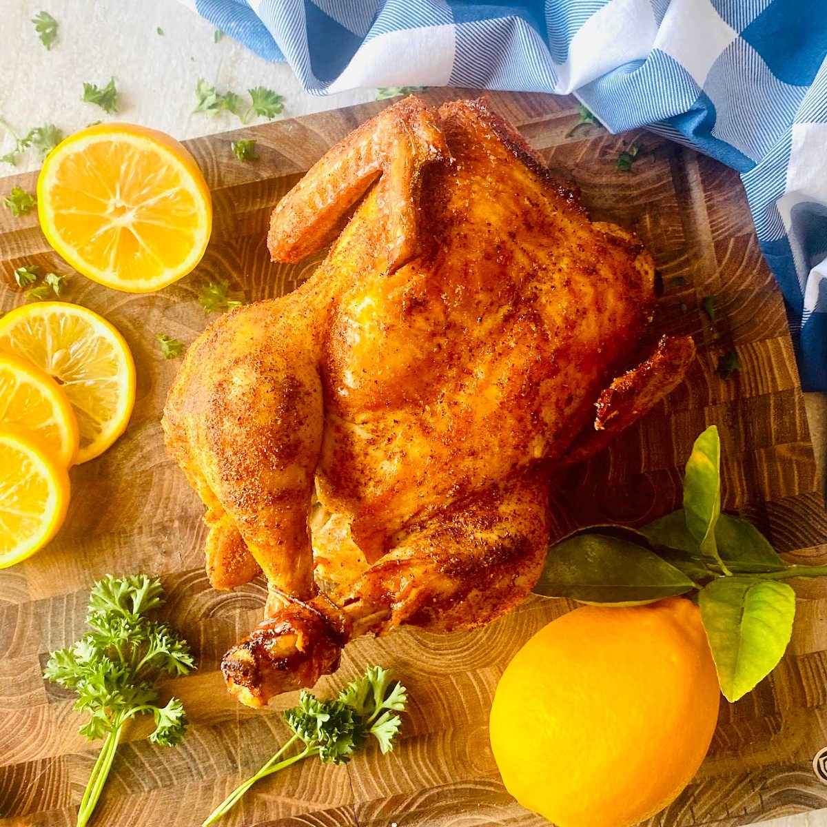 smoked whole chicken on cutting board with lemon and parsley.