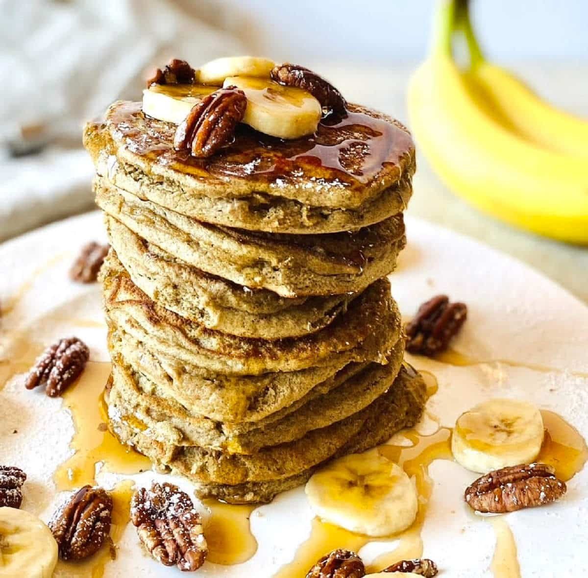 sourdough discard banana pancakes recipe on plate with maple syrup and sliced bananas.
