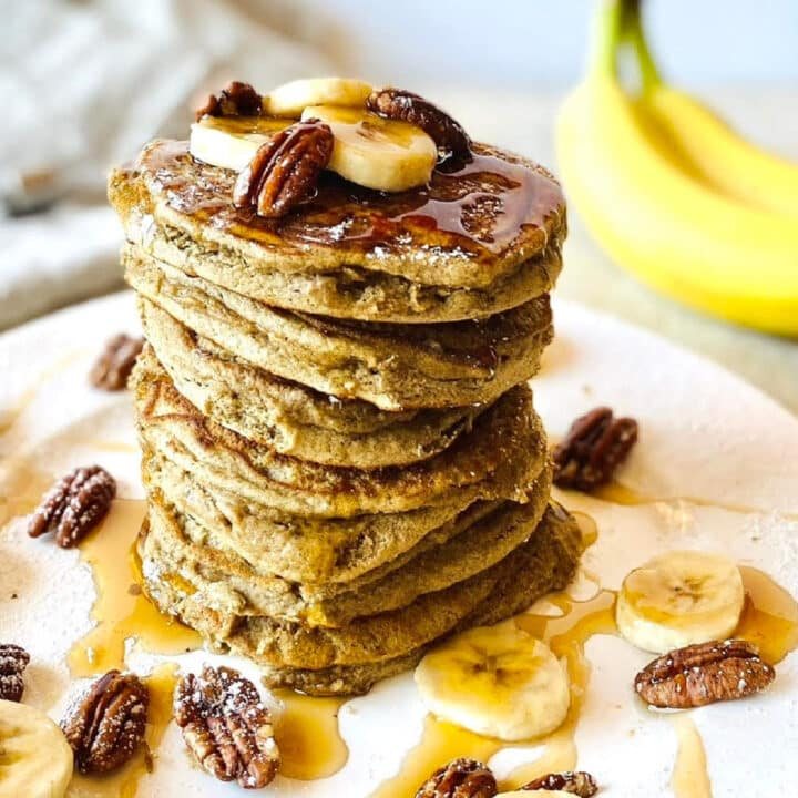 sourdough discard banana pancakes recipe on plate with maple syrup and sliced bananas.
