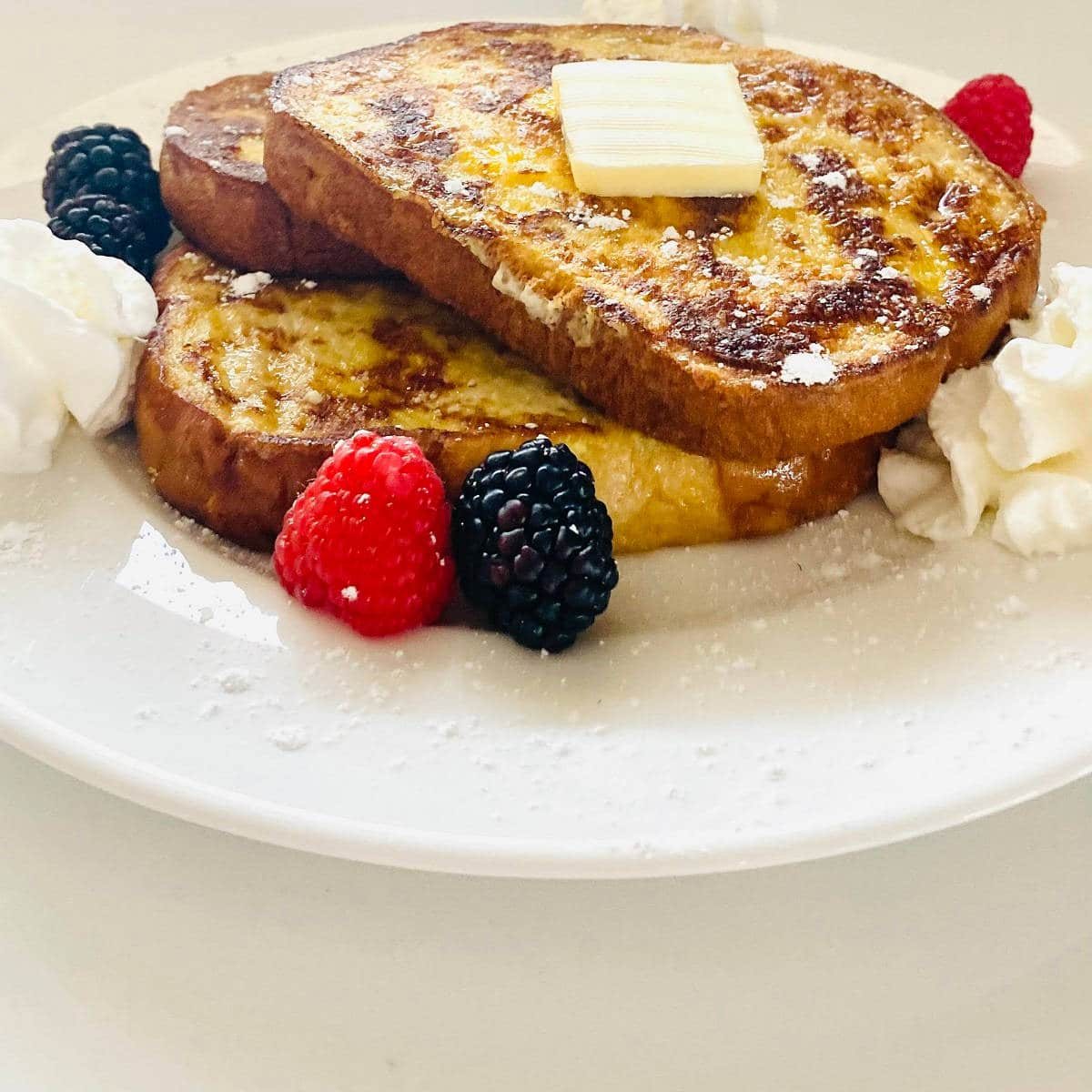 sourdough french toast on plate with butter, whipped cream, blackberries and raspberries