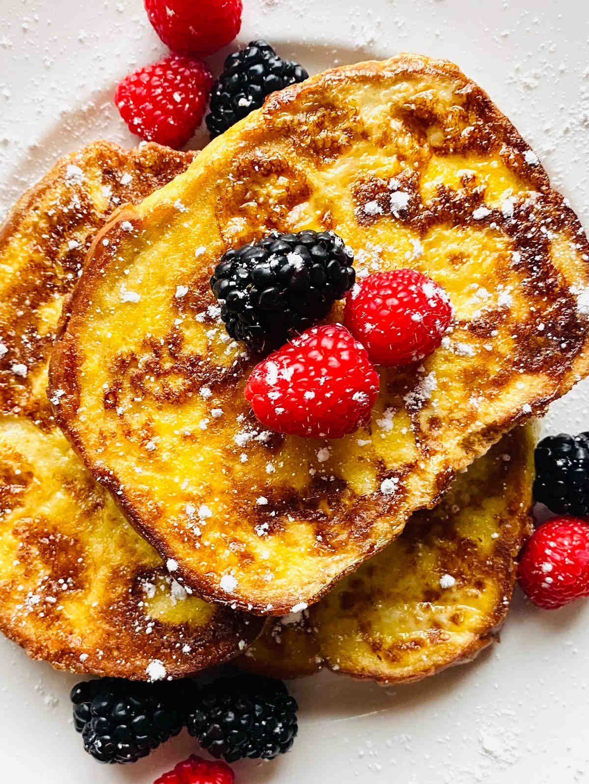 french toast with sourdough bread on plate with berries and powdered sugar