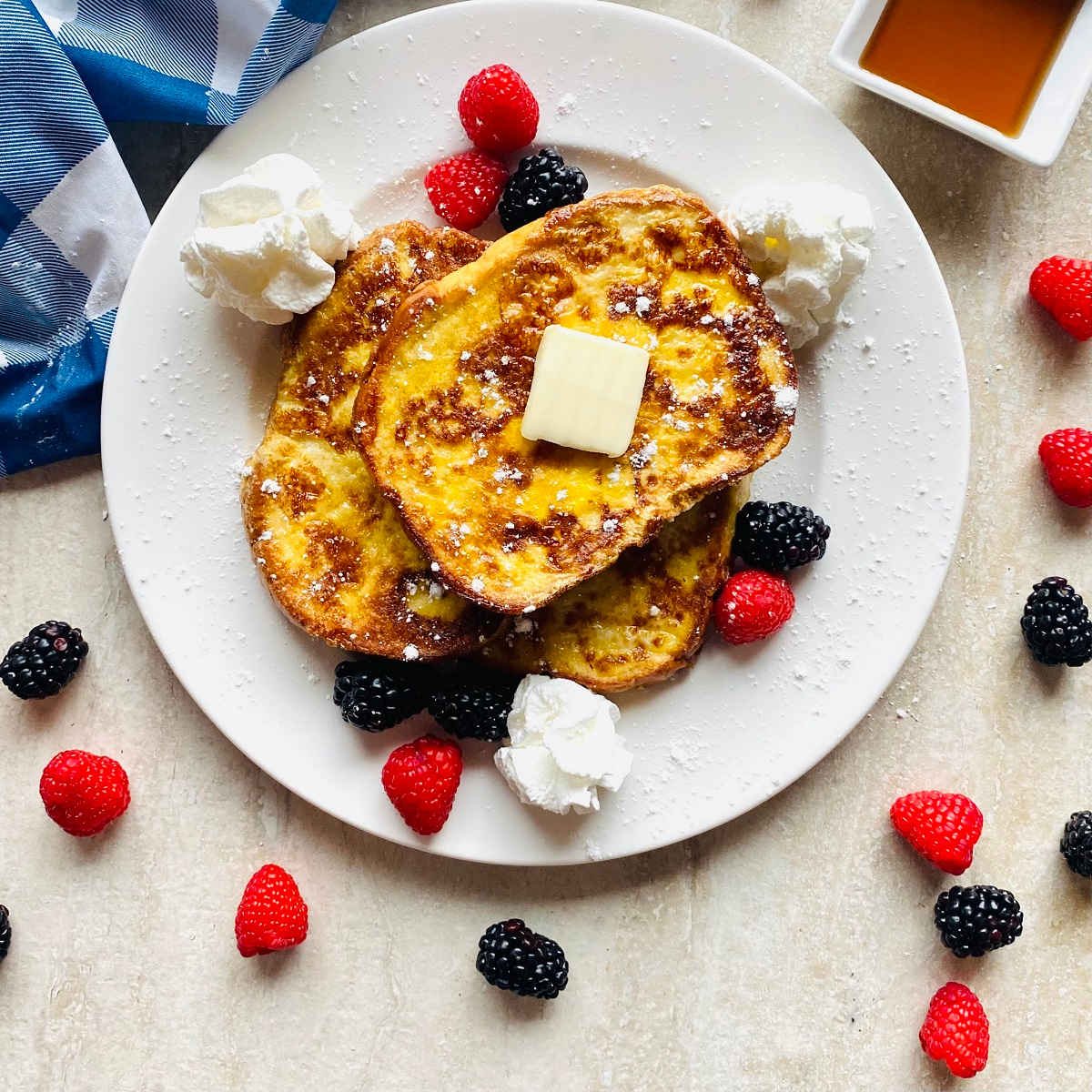 sourdough french toast recipe on plate with berries, whipped cream, butter and maple syrup