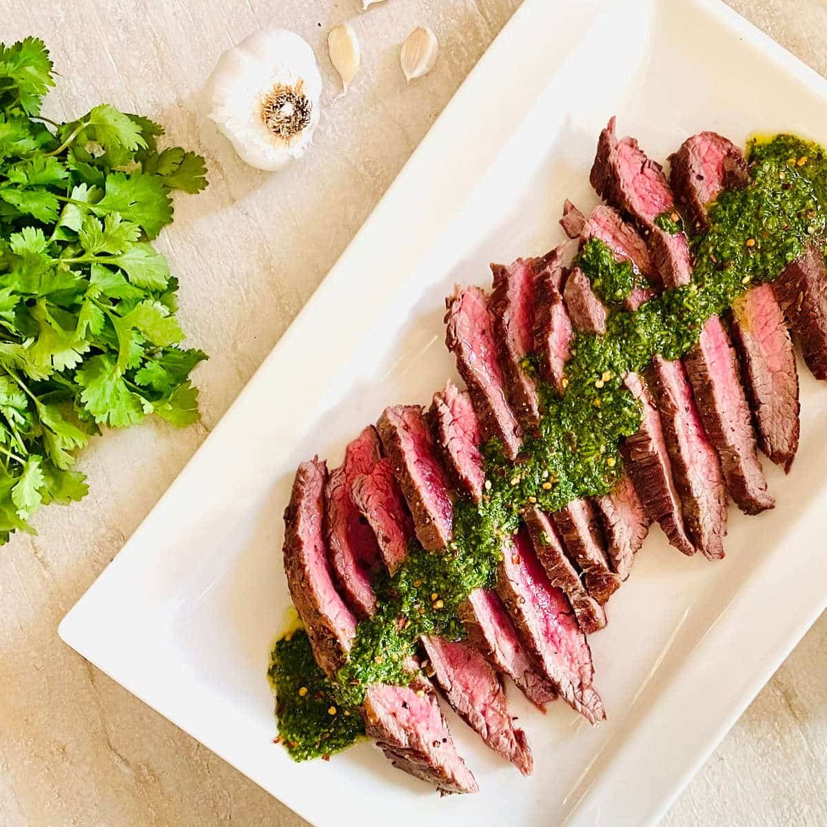 spicy chimichurri over sliced steak next to fresh cilantro and garlic